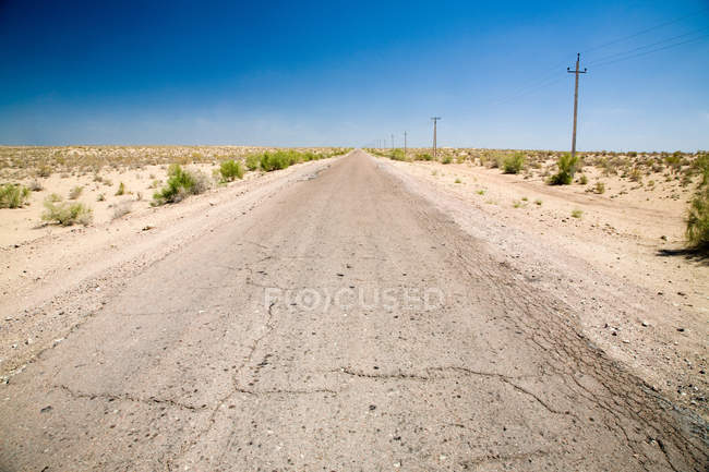 Rissige Straße, die sich unter blauem Himmel durch die Wüste zieht — Stockfoto