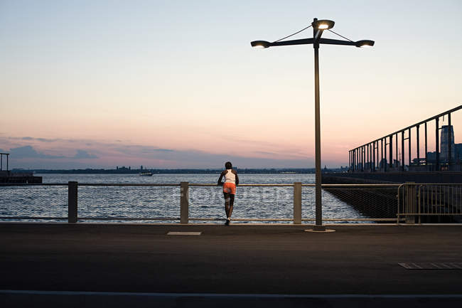 Вид сзади спортсмена, стоящего на мосту у реки — стоковое фото