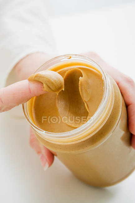 Mujer sacando mantequilla de cacahuete del frasco - foto de stock