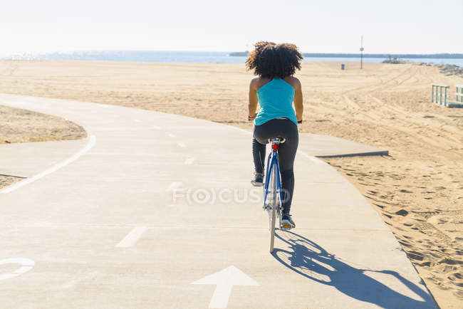 Mid adult woman cycling on pathway at beach, rear view — Stock Photo