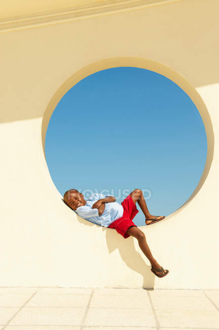Jeune garçon couché dans la fenêtre circulaire — Photo de stock