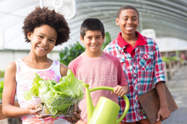 Three children in greenhouse, boy holding watering can — Stock Photo