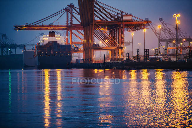 Vista del buque de carga y grúas pórtico en el puerto por la noche, Tacoma, Washington, EE.UU. - foto de stock