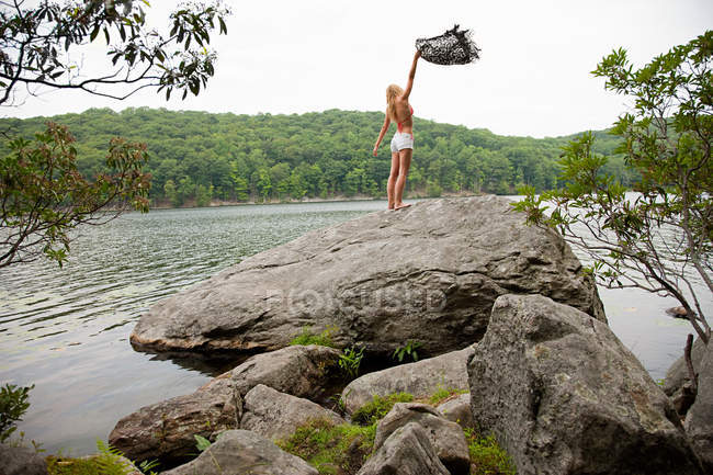 Jovem mulher segurando cobertor na rocha no lago — Fotografia de Stock