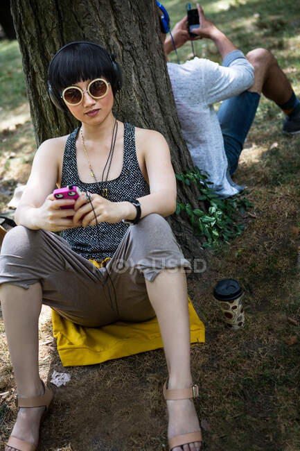Mujer joven apoyada en el tronco del árbol con reproductor de mp3 - foto de stock