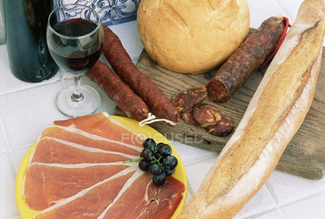 Embutidos con pan y vino en la mesa - foto de stock