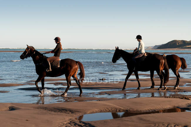 Duas mulheres montando cavalos na praia — Fotografia de Stock