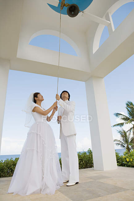 Novia y novio suenan campana de iglesia - foto de stock