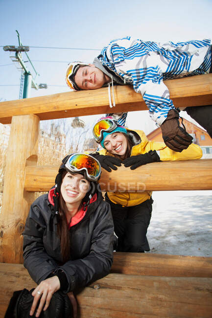 Tres amigos usando ropa de esquí en valla de madera - foto de stock