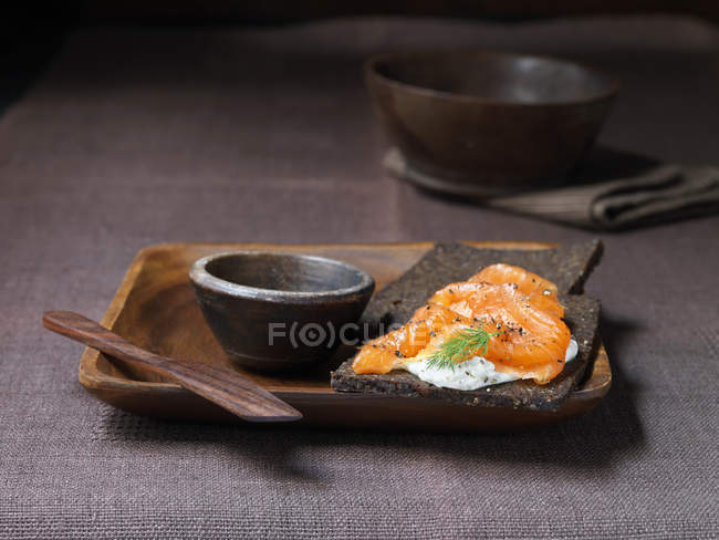 Pumpernickel con queso crema, salmón ahumado con pimienta negra agrietada en plato de madera - foto de stock