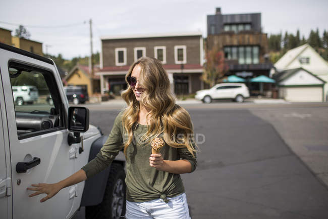 Young woman with long blond hair holding ice cream next to jeep — Stock Photo