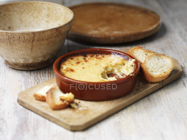 Bowl of welsh rarebit bake with toasted bread on wooden chopping board — Stock Photo