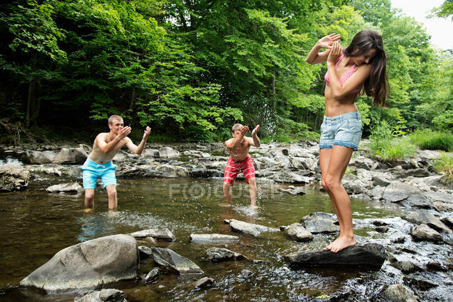 Dois homens jovens salpicando amigo feminino no rio — Fotografia de Stock