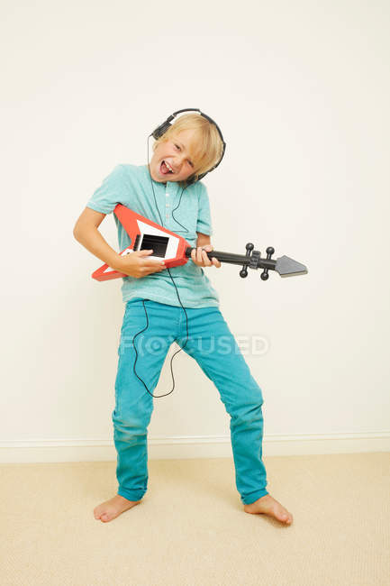 Menino usando fones de ouvido tocando guitarra — Fotografia de Stock