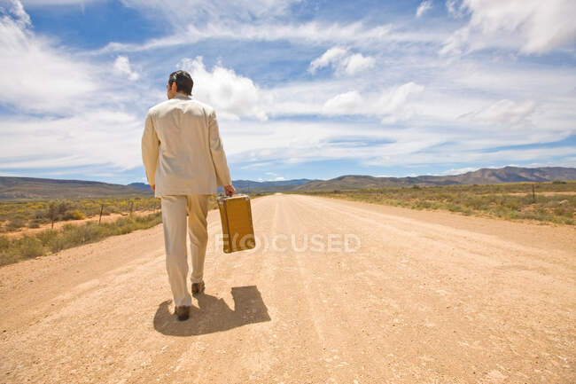 Visão traseira do homem de terno andando onb a estrada com bagagem — Fotografia de Stock