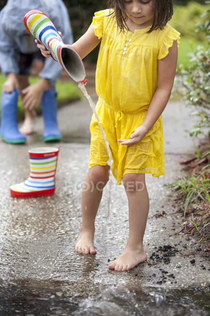 Fille verser de l'eau de bottes en caoutchouc dans la flaque d'eau de pluie — Photo de stock