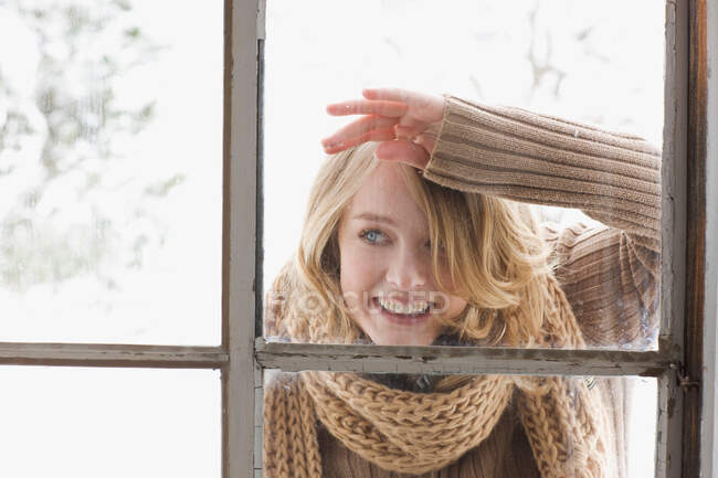 Junge Frau blickt durch Fenster — Stockfoto