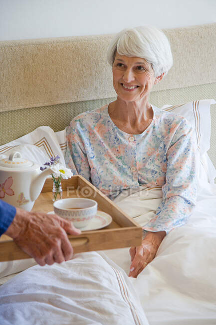 Um homem sênior trazendo um café da manhã de uma mulher sênior — Fotografia de Stock