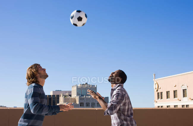Friends on roof top heading football — Stock Photo
