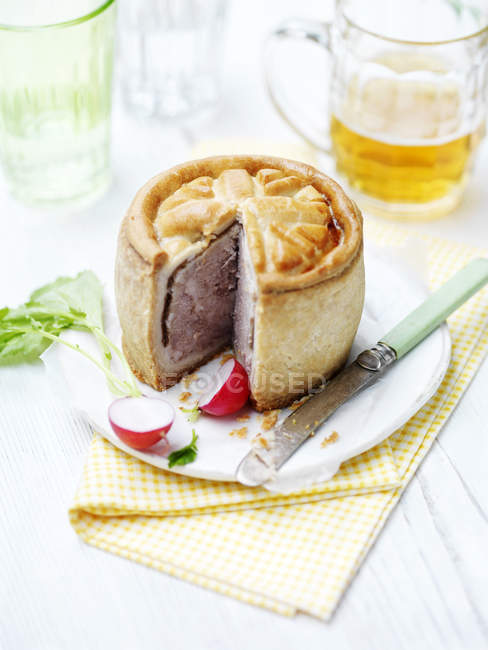 Pork pie with radishes and knife on plate — Stock Photo