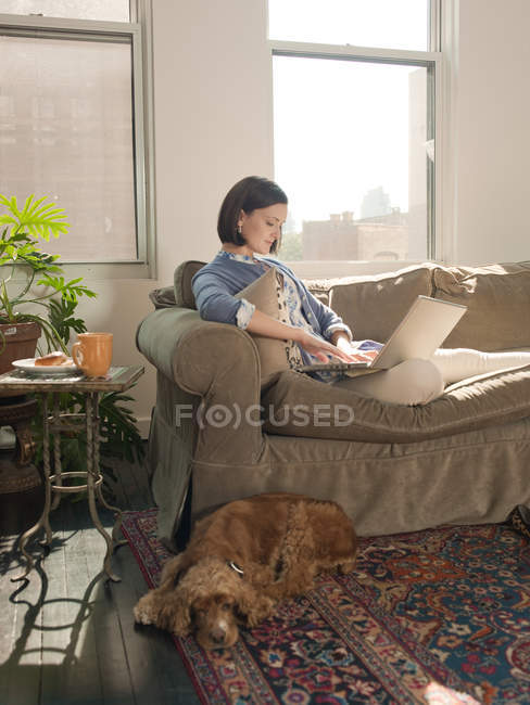 Жінка розслабляється на дивані і використовує ноутбук — стокове фото