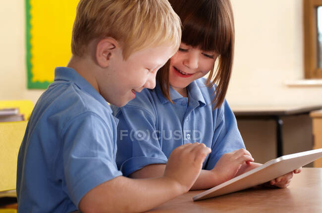 Two school children using computer notebook in classroom — Stock Photo