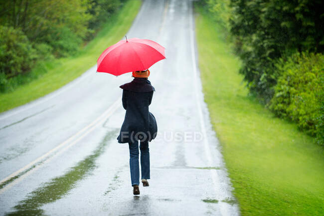Frau mit rotem Regenschirm auf leerer Straße — Stockfoto