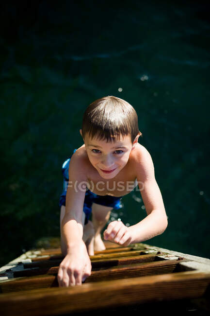 Boy climbing up ladder from the sea — Stock Photo