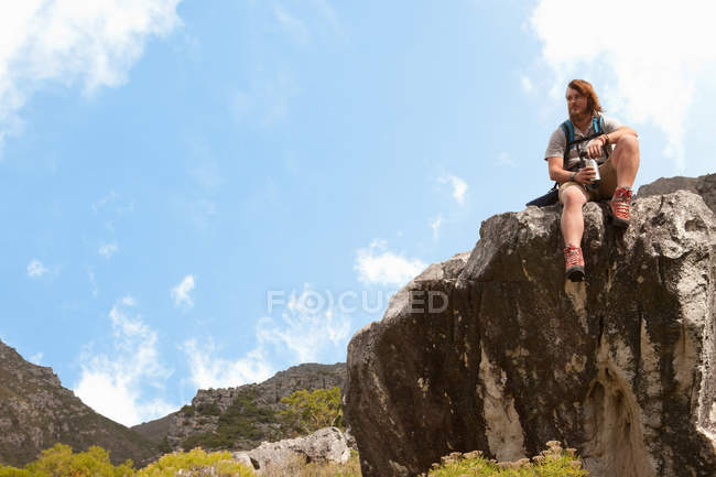 Randonneur assis sur une formation rocheuse avec fiole à boire — Photo de stock
