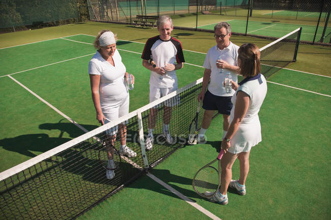 Adultos mayores y mayores disfrutando de la bebida en pista de tenis - foto de stock