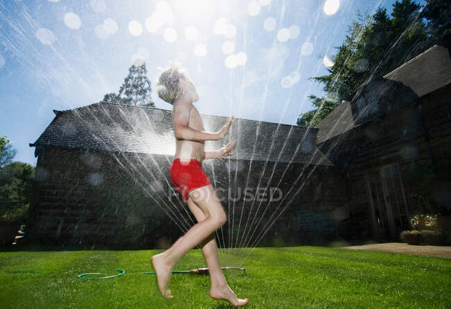 Boy running through sprinklers — Stock Photo