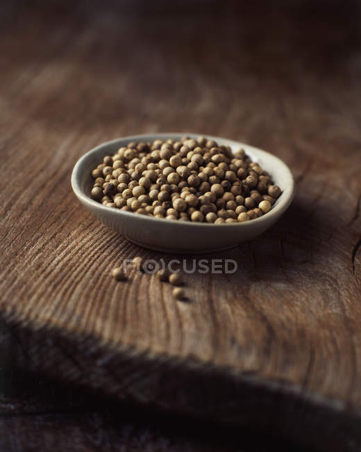 Ceramic bowl of white peppercorns on wooden surface — Stock Photo