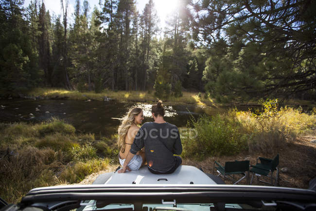 Rear view of romantic young couple sitting on jeep hood at riverside, Lake Tahoe, Nevada, USA — Stock Photo