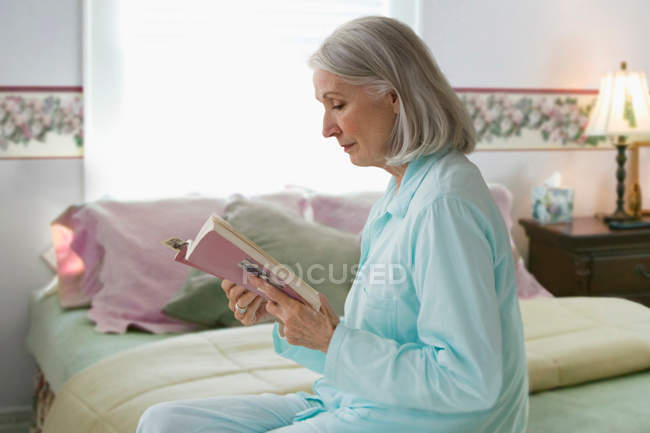 Seniorin liest Buch im Schlafzimmer — Stockfoto