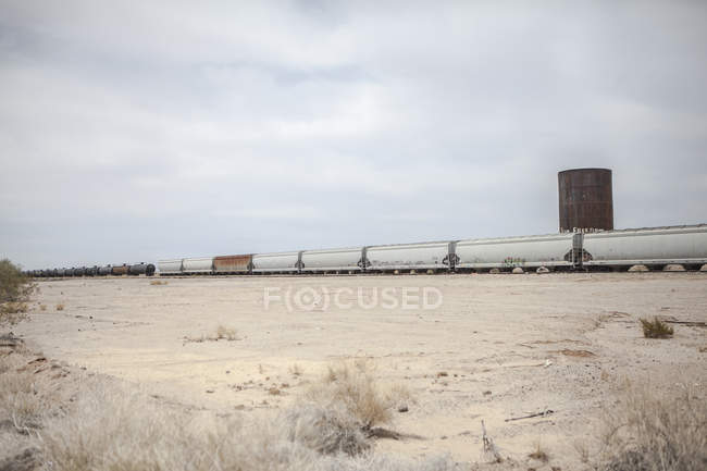 Diminishing view of freight train in desert under cloudy sky — Stock Photo