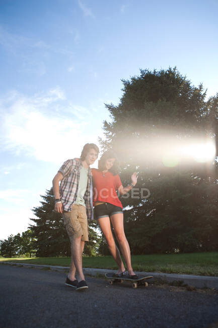 Teenage boy helping girlfriend ride skateboard — Stock Photo