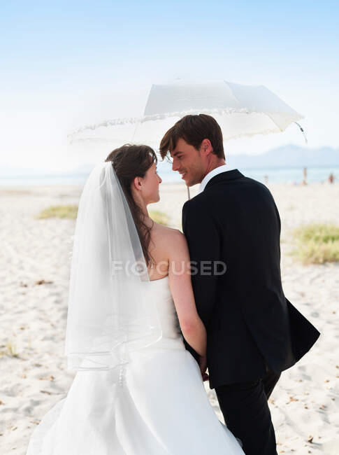 Bride and groom walking under parasol — Stock Photo