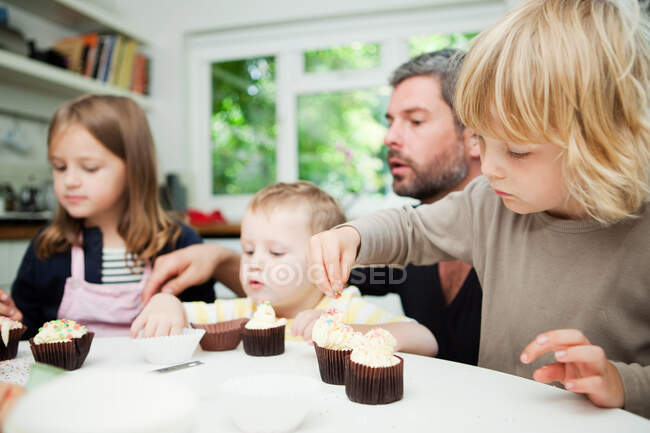 Mitte erwachsener Mann und Familie dekorieren Cupcakes — Stockfoto