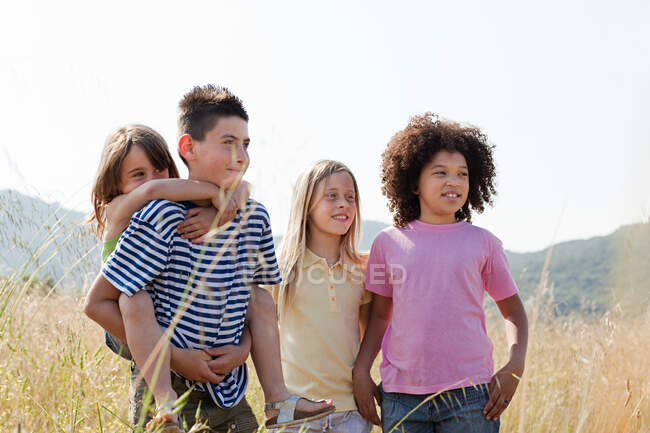 Cuatro amigos en el campo, la chica más joven teniendo cerdito espalda - foto de stock