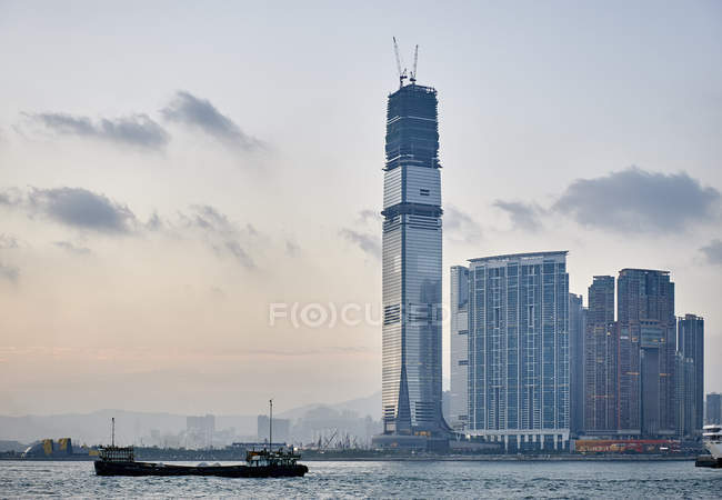 Distant view of barge and skyscrapers against sunset sky, Tsim Sha Tsui, Hong Kong — Stock Photo
