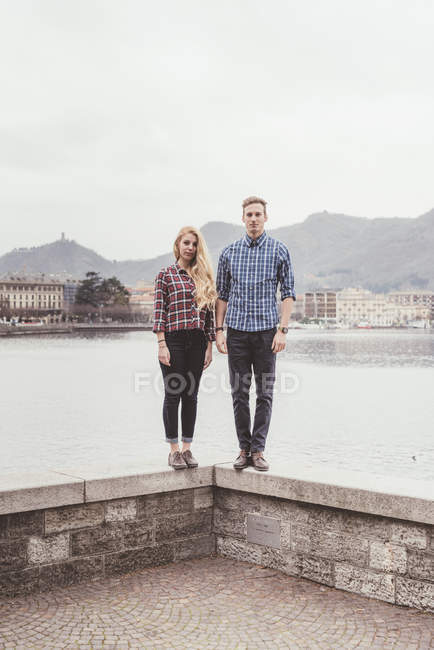 Portrait de jeune couple debout sur le mur du port, Lac de Côme, Italie — Photo de stock