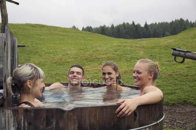 Quatro amigos adultos rindo enquanto relaxam na banheira de hidromassagem rural, Sattelbergalm, Tirol, Áustria — Fotografia de Stock