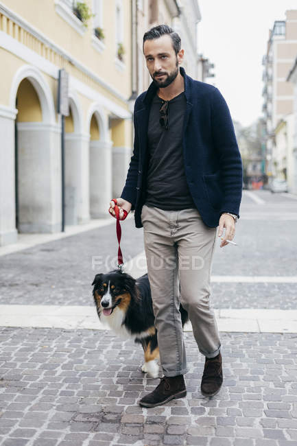 Mitte erwachsener Mann geht mit Hund in gepflasterter Stadtstraße spazieren — Stockfoto