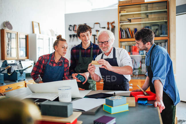 Seniorchef eines Männerworkshops zeigt jungen Männern und Frauen in der Buchkunstwerkstatt Materialien — Stockfoto
