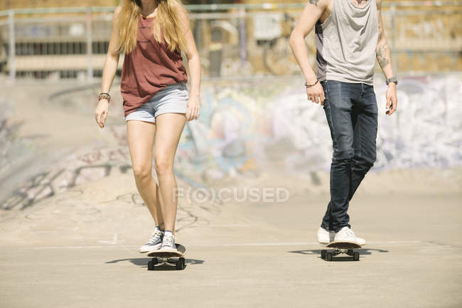 Neck down view of female and male skateboarders skateboarding in skatepark — Stock Photo