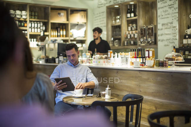 Чоловік сидить у кафе, переглядаючи цифровий планшет — стокове фото