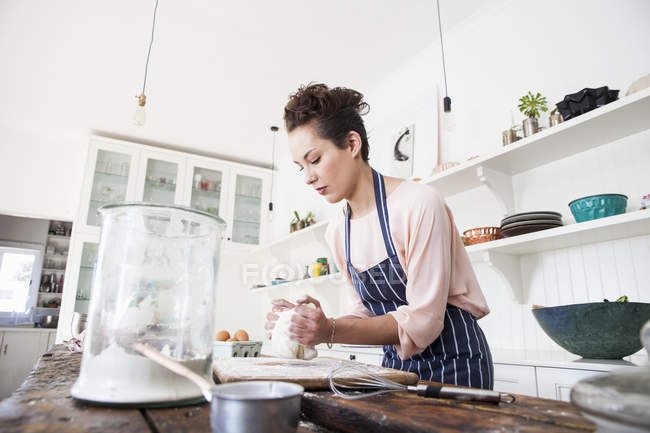 Jovem mulher amassar massa de farinha no balcão da cozinha — Fotografia de Stock