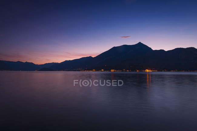 View of silhouetted mountains and illuminated coastal buildings at night — Stock Photo