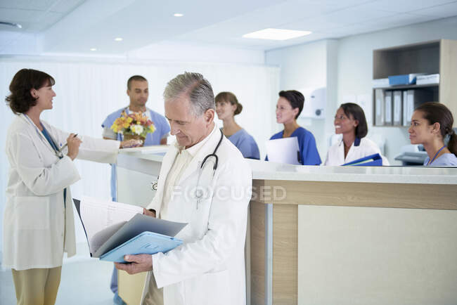 Senior doctor reading medical notes at hospital nurses station — Stock Photo