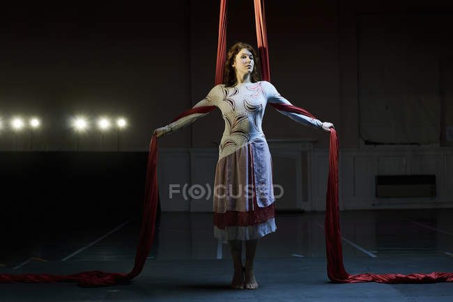 Портрет молодой женщины-акробатки, стоящей между красными шелковыми веревками — стоковое фото